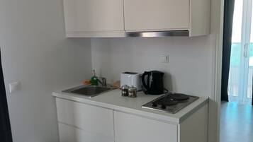 A compact kitchenette with a sink, a toaster, a kettle, and a trash bin.