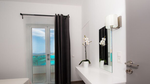 A modern bathroom with a glass door leading to a balcony, a white sink with a mirror, and a potted orchid. - Aestas Apts (Chania)