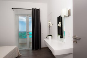 A modern bathroom with a glass door leading to a balcony, a white sink with a mirror, and a potted orchid. - Aestas Apts (Chania)