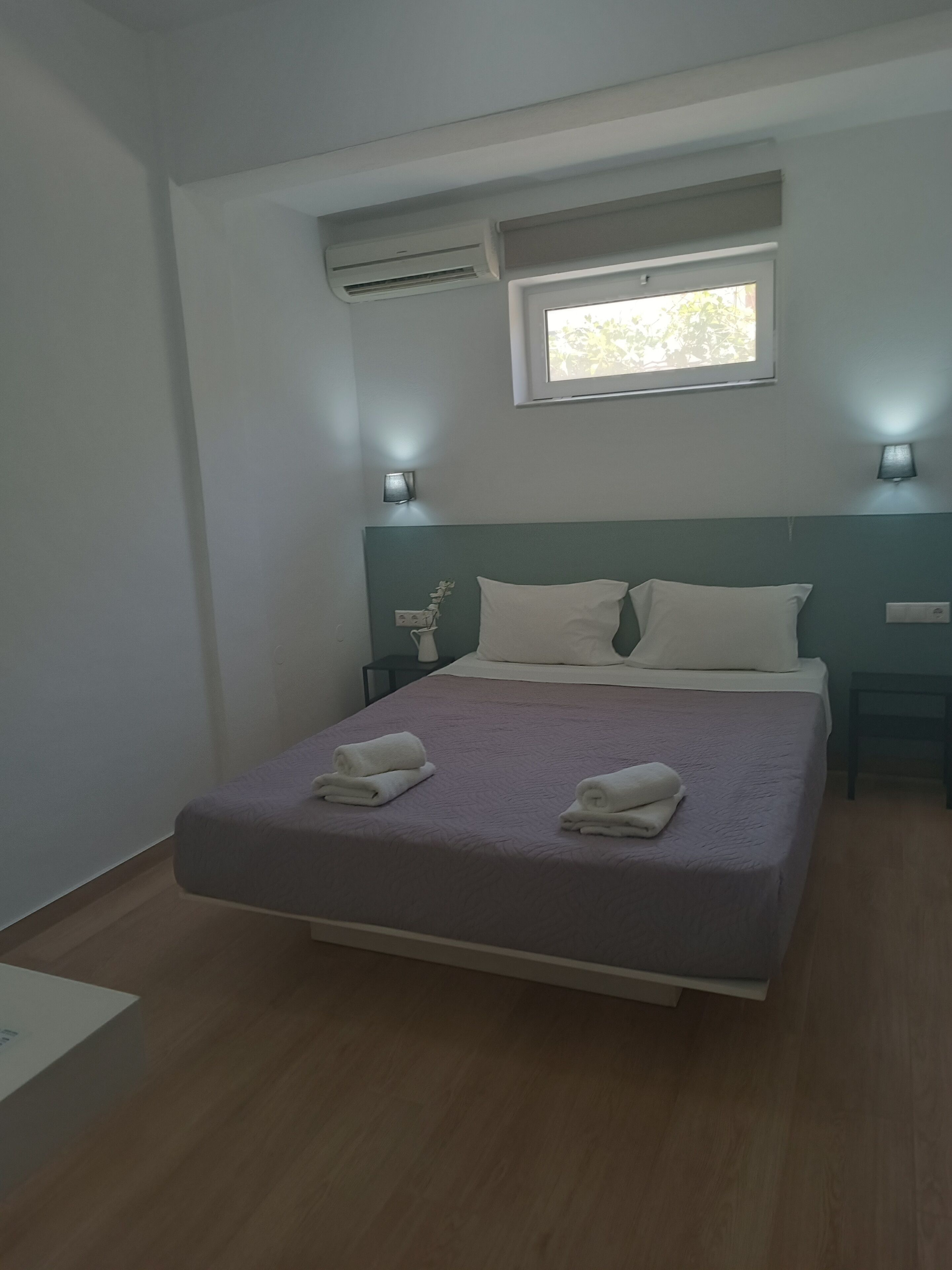 Ein Schlafzimmer mit einem Bett, zwei Nachttischen, einem Fenster und einer Klimaanlage.