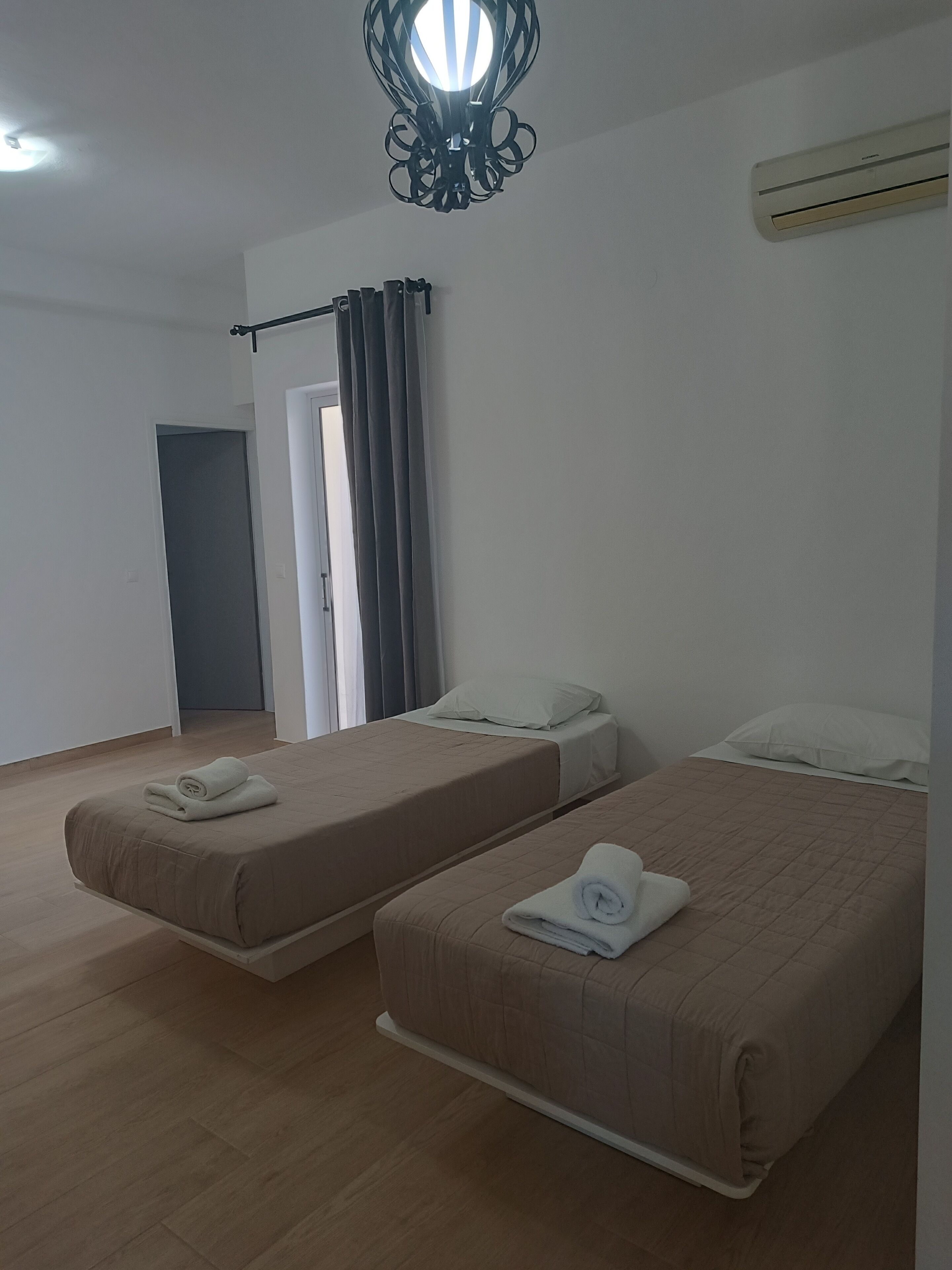 Une chambre avec deux lits, un luminaire au plafond, un appareil de climatisation et une porte.