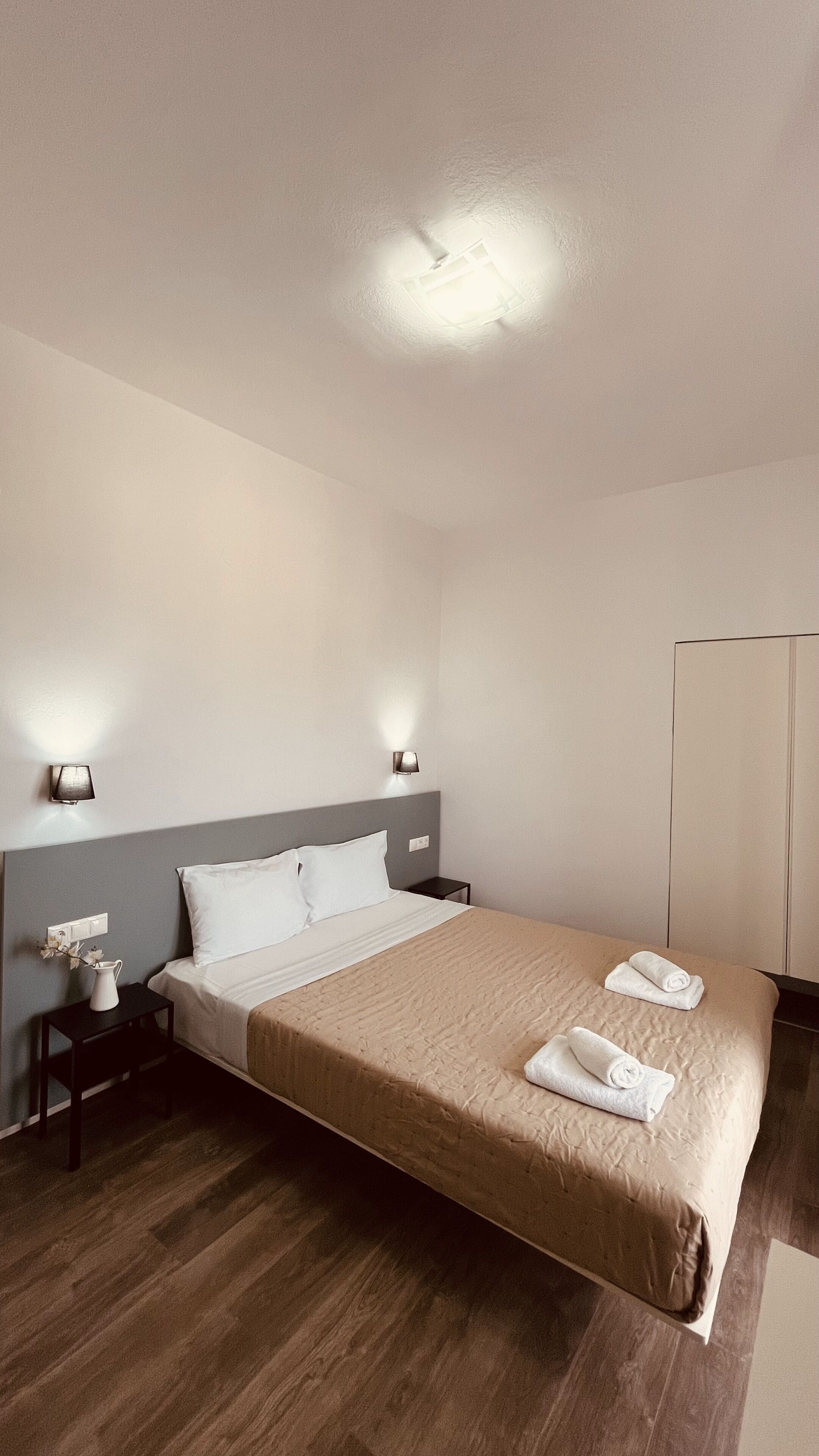A hotel room with a large bed, bedside lamps, a nightstand, a wooden floor, and a wardrobe.