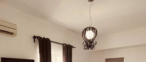 Una camera d'albergo con un letto, una scrivania, una sedia, una televisione, una finestra con tende, una porta e una lampada a soffitto.