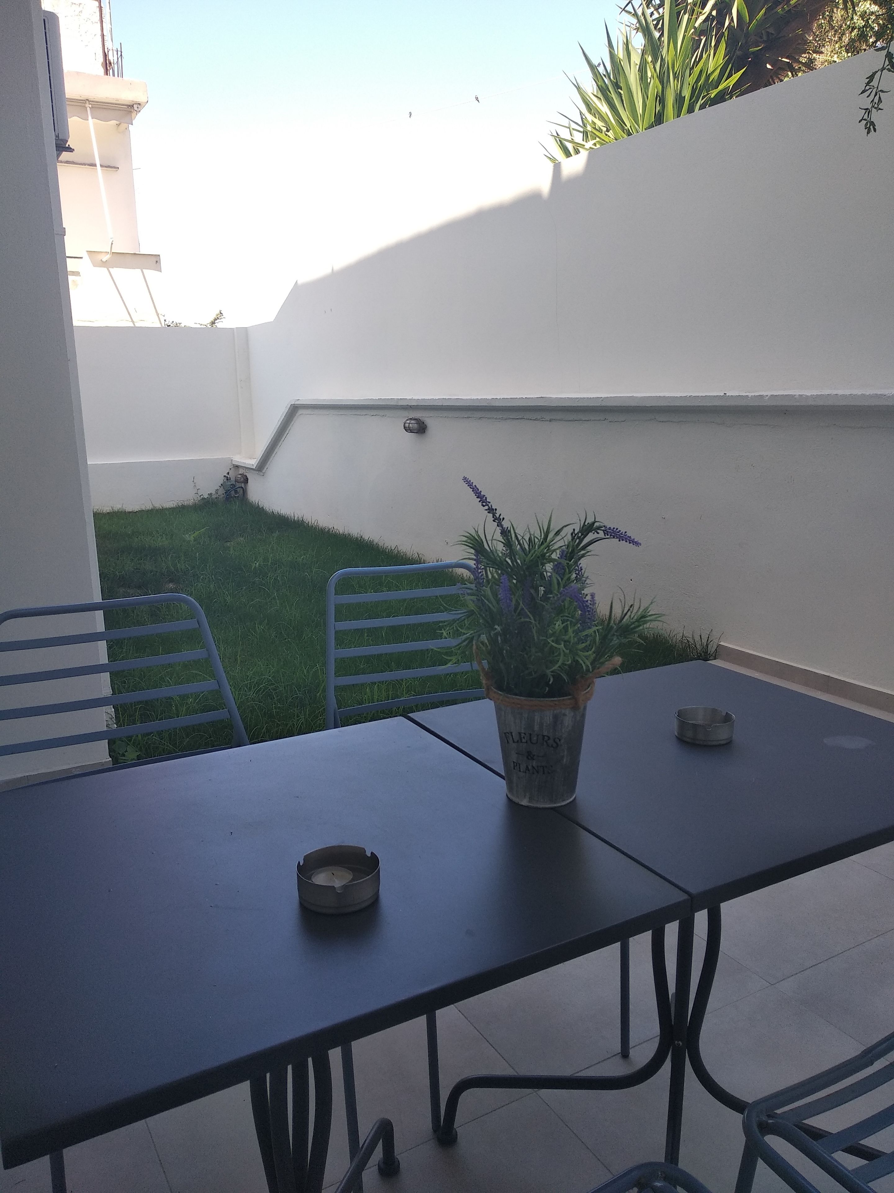 Une terrasse avec une table, des chaises, un pot de fleurs et une bougie.