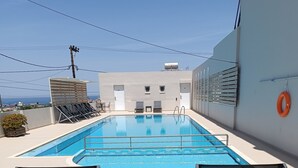 A rooftop pool with a clear view of the city skyline, two lounge chairs, and a small table. - Aestas Apts (Chania)