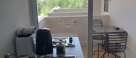 A modern kitchen with a sink, a coffee maker, and a kettle. There is a small table with chairs and a view of greenery outside.