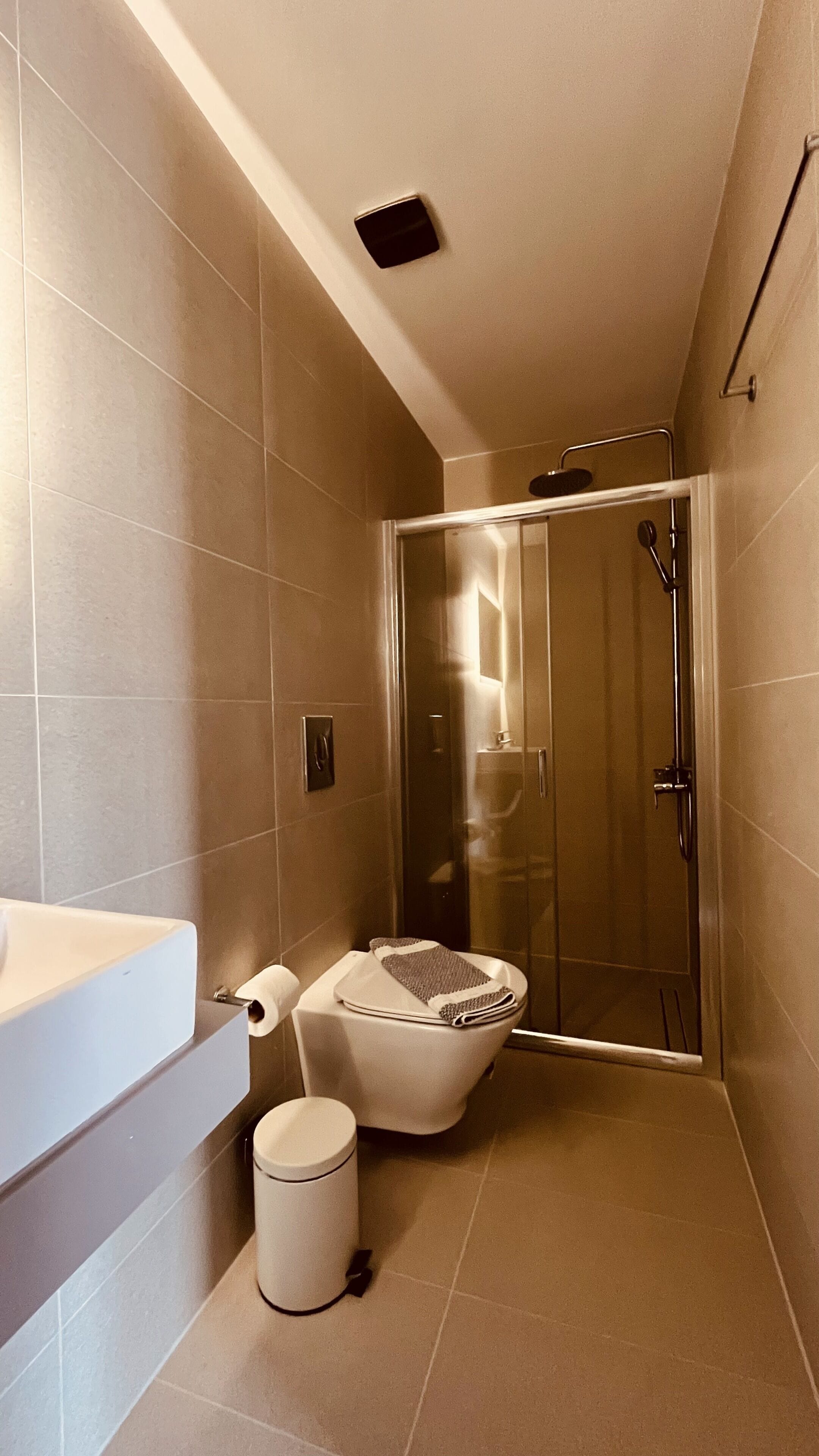 A bathroom with a toilet, a trash bin, a shower enclosure, and a sink.