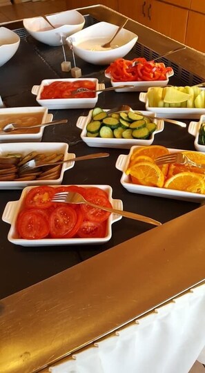 A buffet table with various food items including sliced tomatoes, cucumbers, oranges, and other vegetables. - Landhotel Basler Hof (Lauterbach)