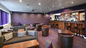 A hotel lobby with sofas, tables, a bar area, and a patterned wall. - Lancaster Hotel (Uxbridge)