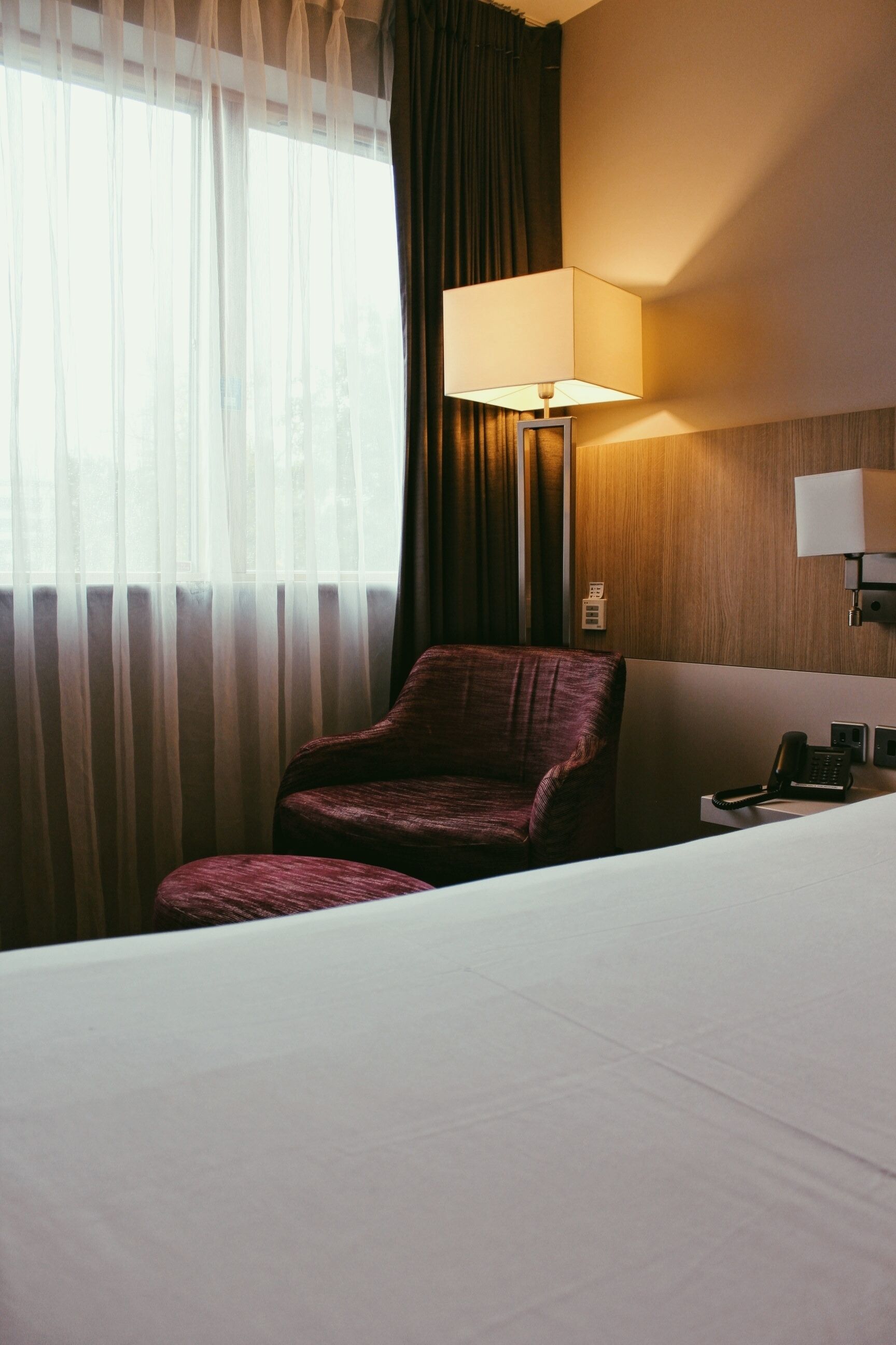 A hotel room with a bed, a chair, a lamp, and a telephone.
