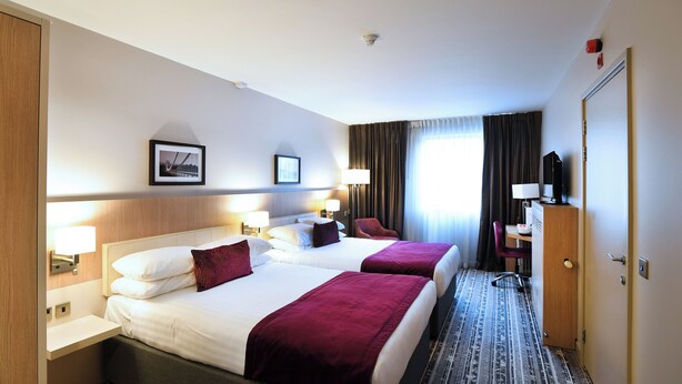A hotel room with two beds, a desk, a chair, and a television. - Lancaster Hotel (Uxbridge)