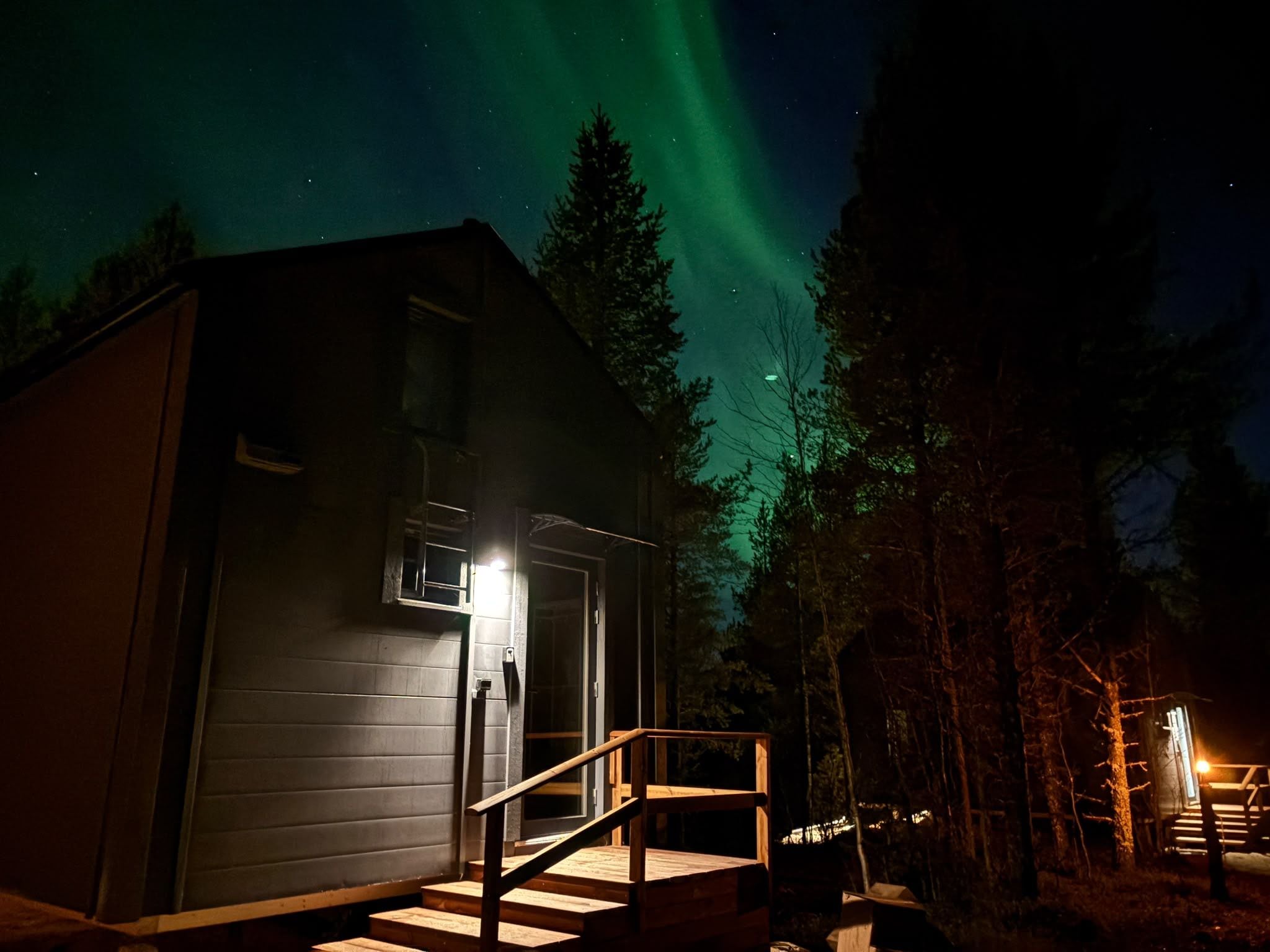 A cabin with a wooden staircase leading to a door, surrounded by trees.