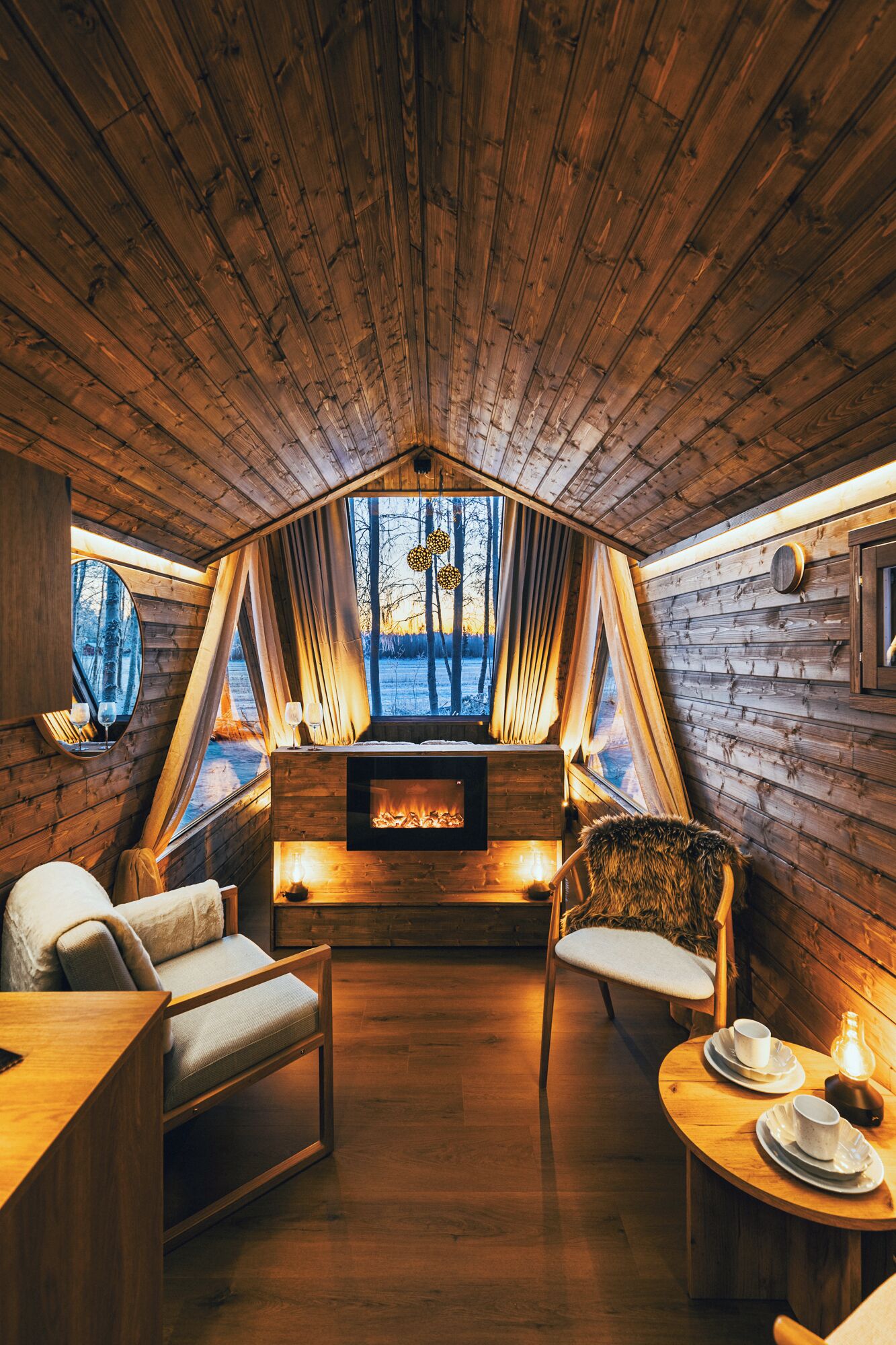 Un interior cálido y rústico de madera, con chimenea, zona de estar y ventanas amplias que dan al exterior.
