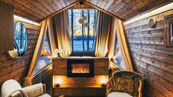 Un interior cálido y rústico de madera, con chimenea, zona de estar y ventanas amplias que dan al exterior.
