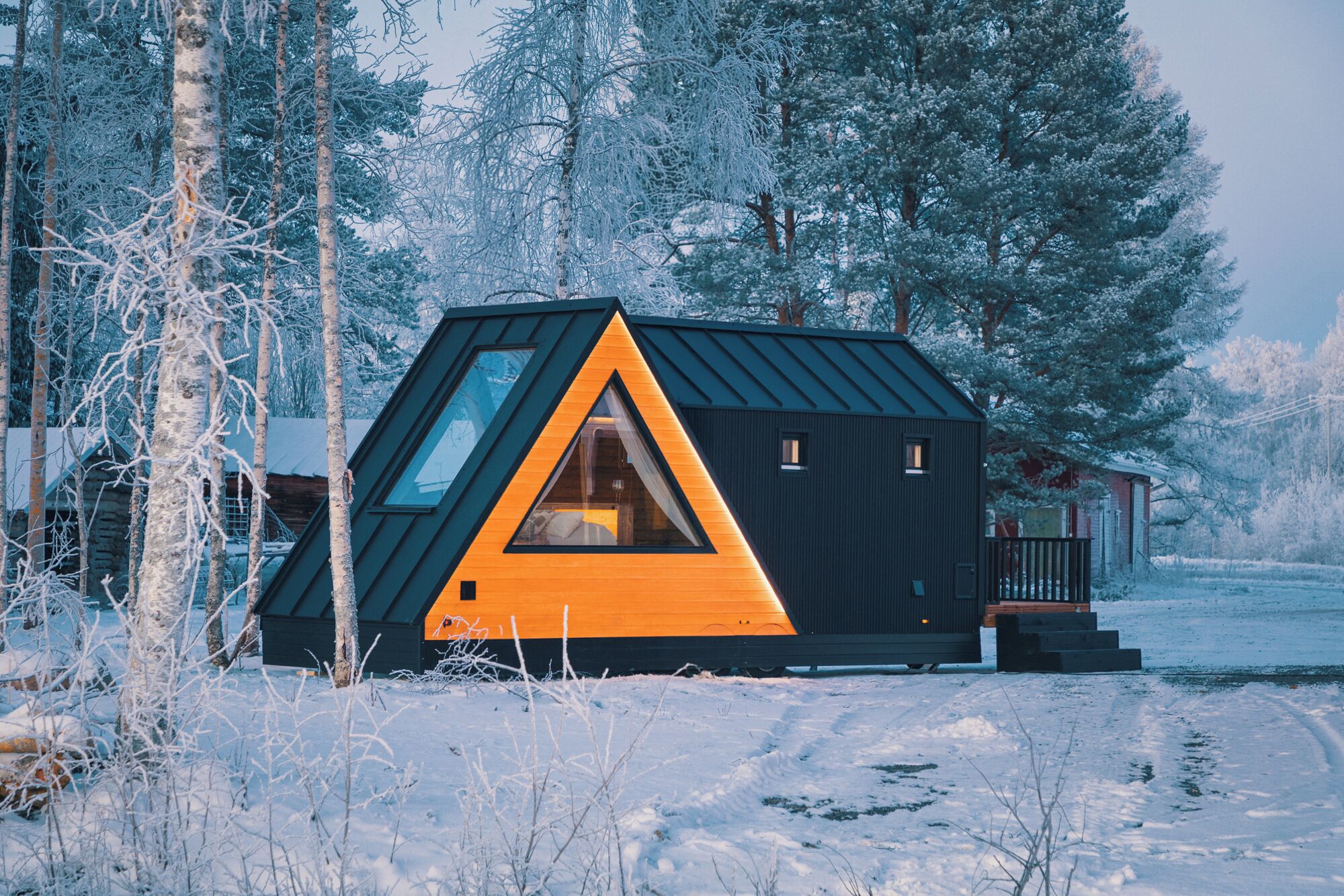 Una cabaña con un ventanal triangular, rodeada de árboles cubiertos de nieve.