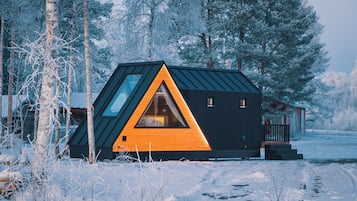 Una cabaña con un ventanal triangular, rodeada de árboles cubiertos de nieve.