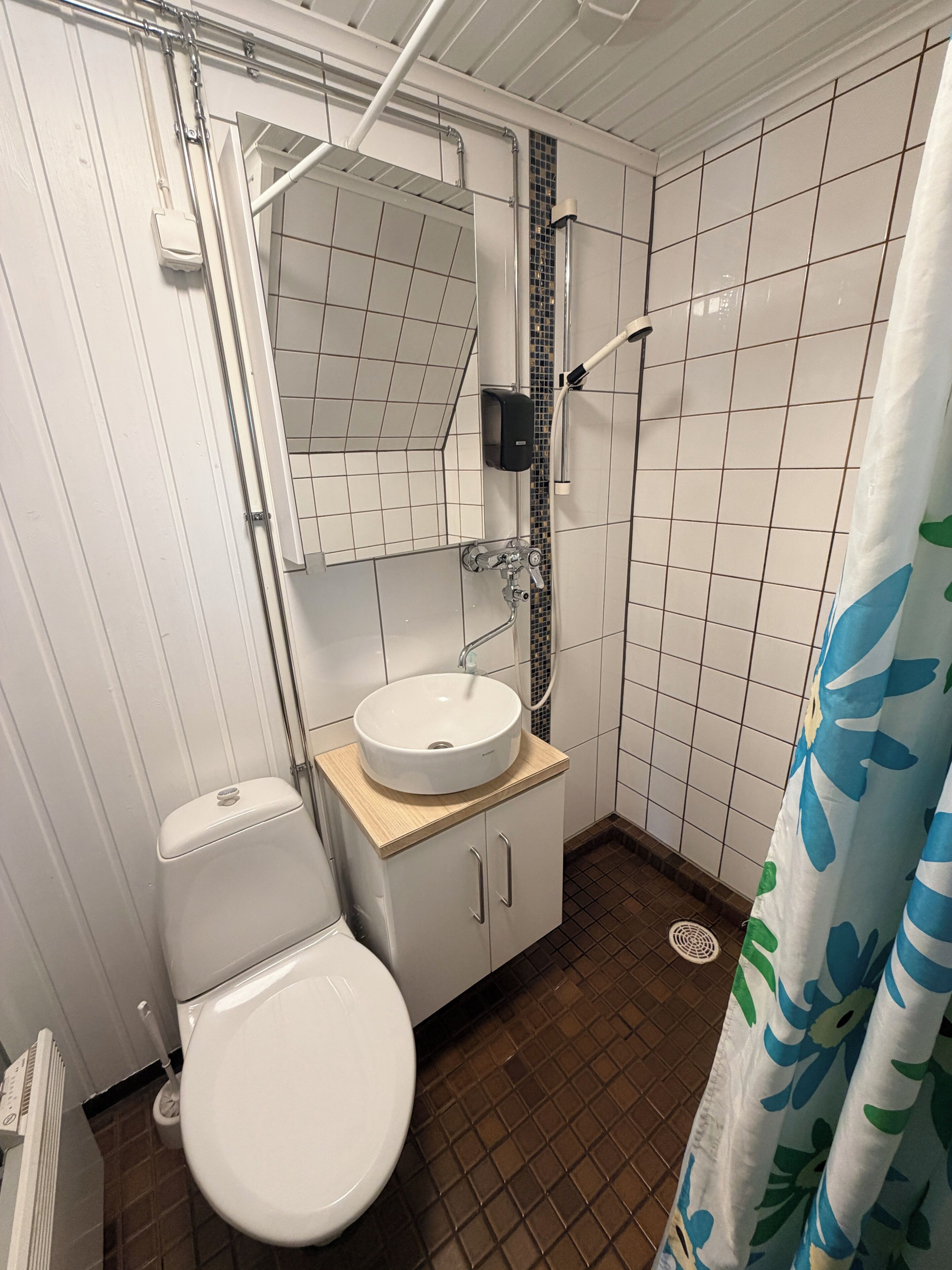 Une salle de bain équipée d’un WC, d’un lavabo, d’un miroir, d’une douche et de murs carrelés.