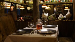 A table set for dining with plates, cutlery, and glasses, in a dimly lit restaurant with wooden decor and hanging lamps. - Tankavaara Gold Village (Sodankyla)