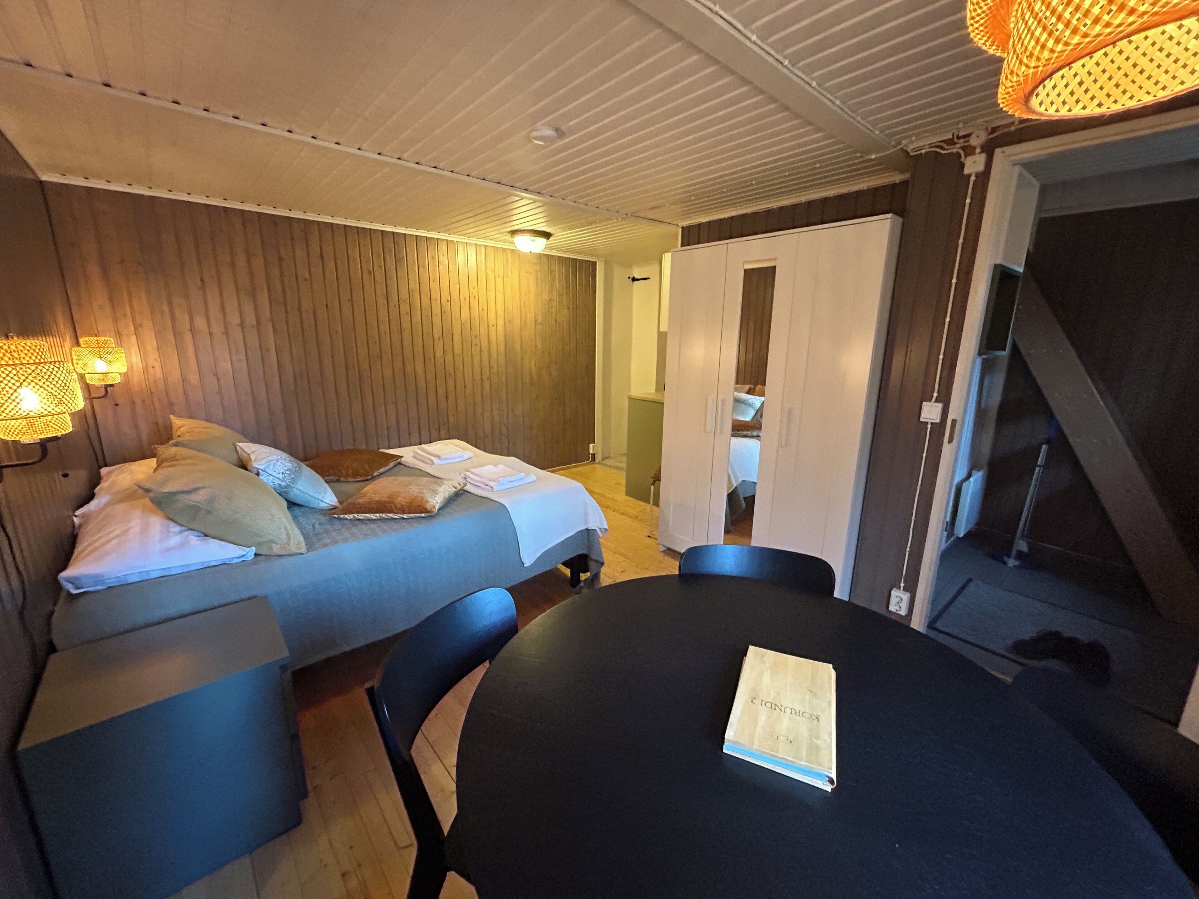 A room with a bed, a table, and a chair. There is a book on the table.