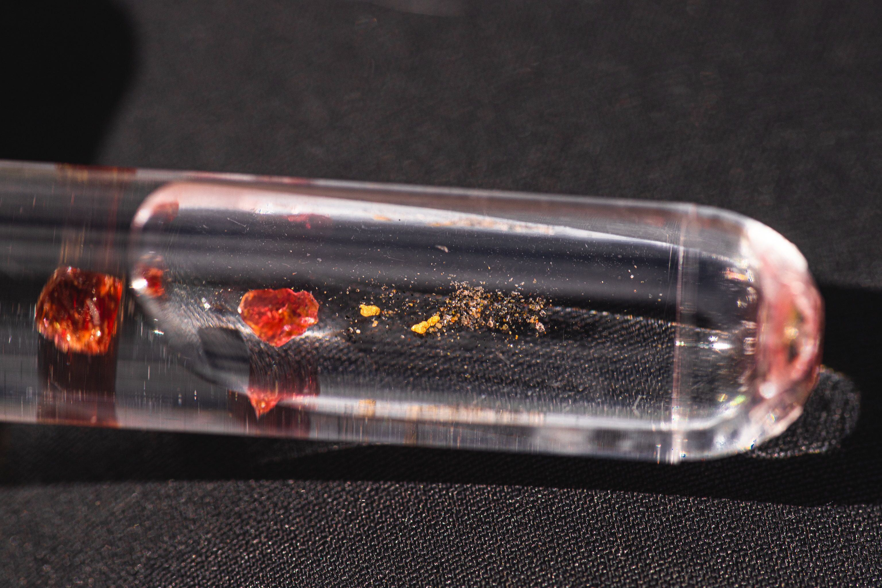 Un tubo de vidrio transparente con partículas visibles y un pequeño objeto rojo en su interior.