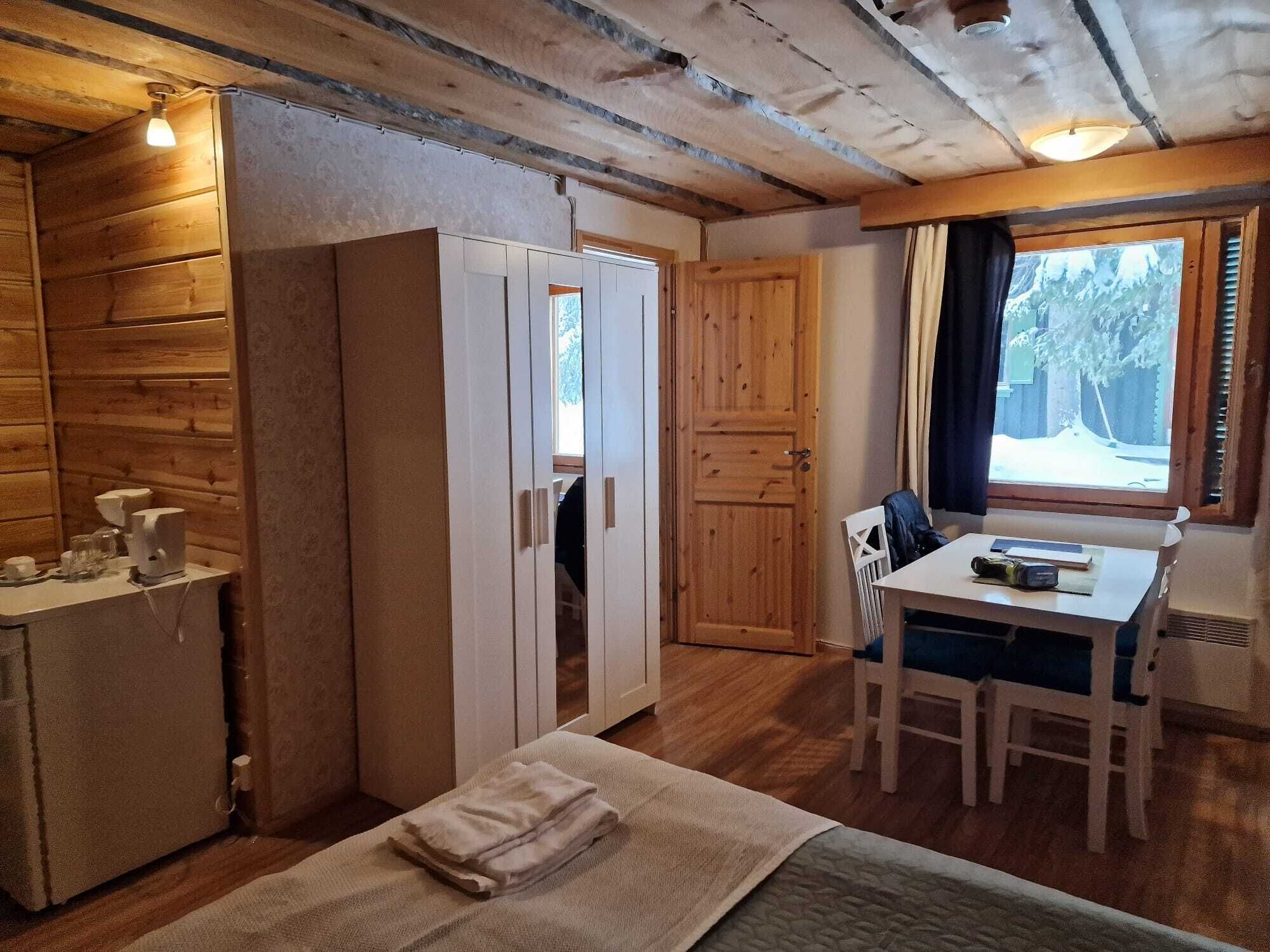 A cozy cabin interior with wooden walls, a dining area, and a window with a view of trees.