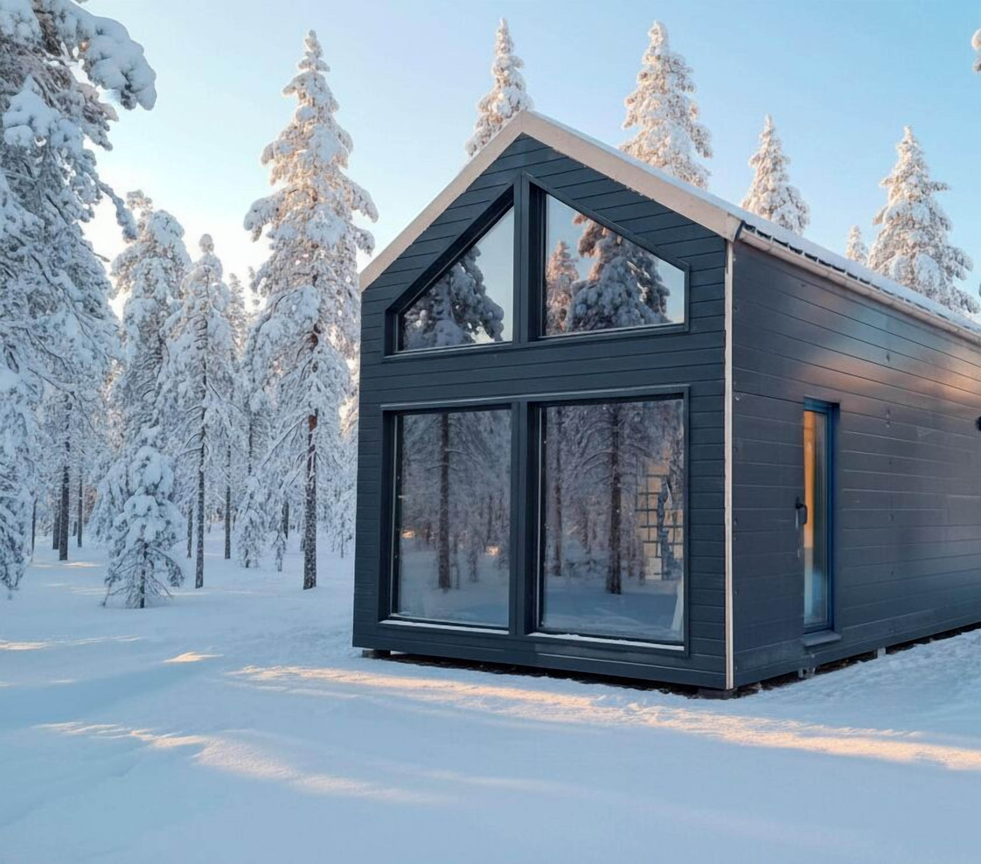 A modern cabin with a large glass window and a sloped roof, surrounded by snow-covered trees.
