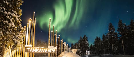 A snow-covered landscape with a sign reading "TANKAVAARA" and a view of the Northern Lights.
