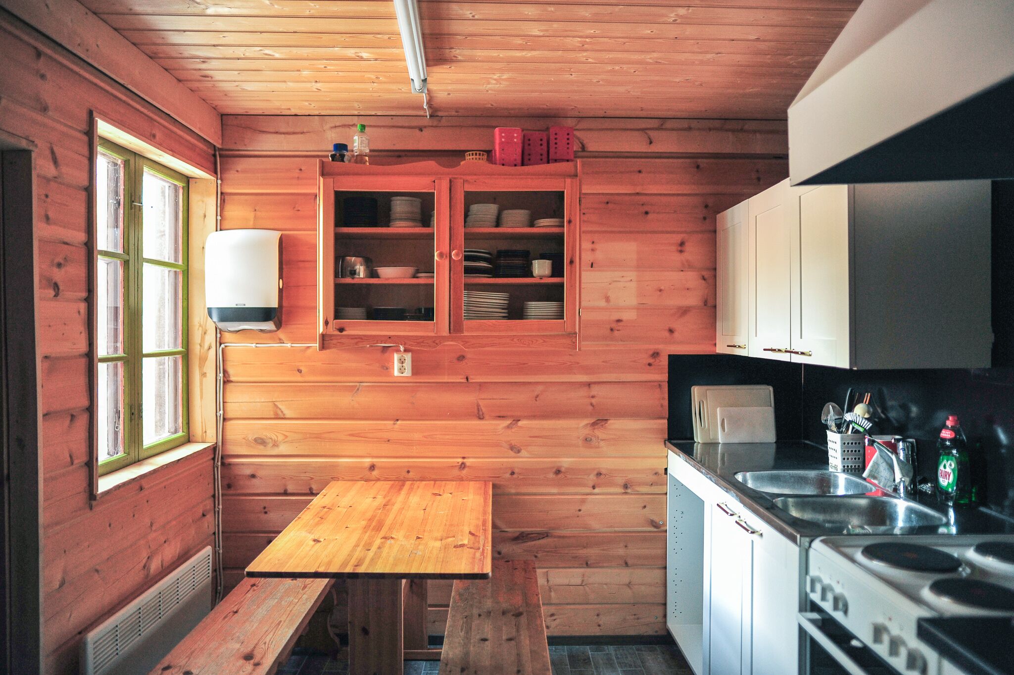 L’intérieur d’une cabane en bois, avec une table en bois, un banc, un évier et un poêle.