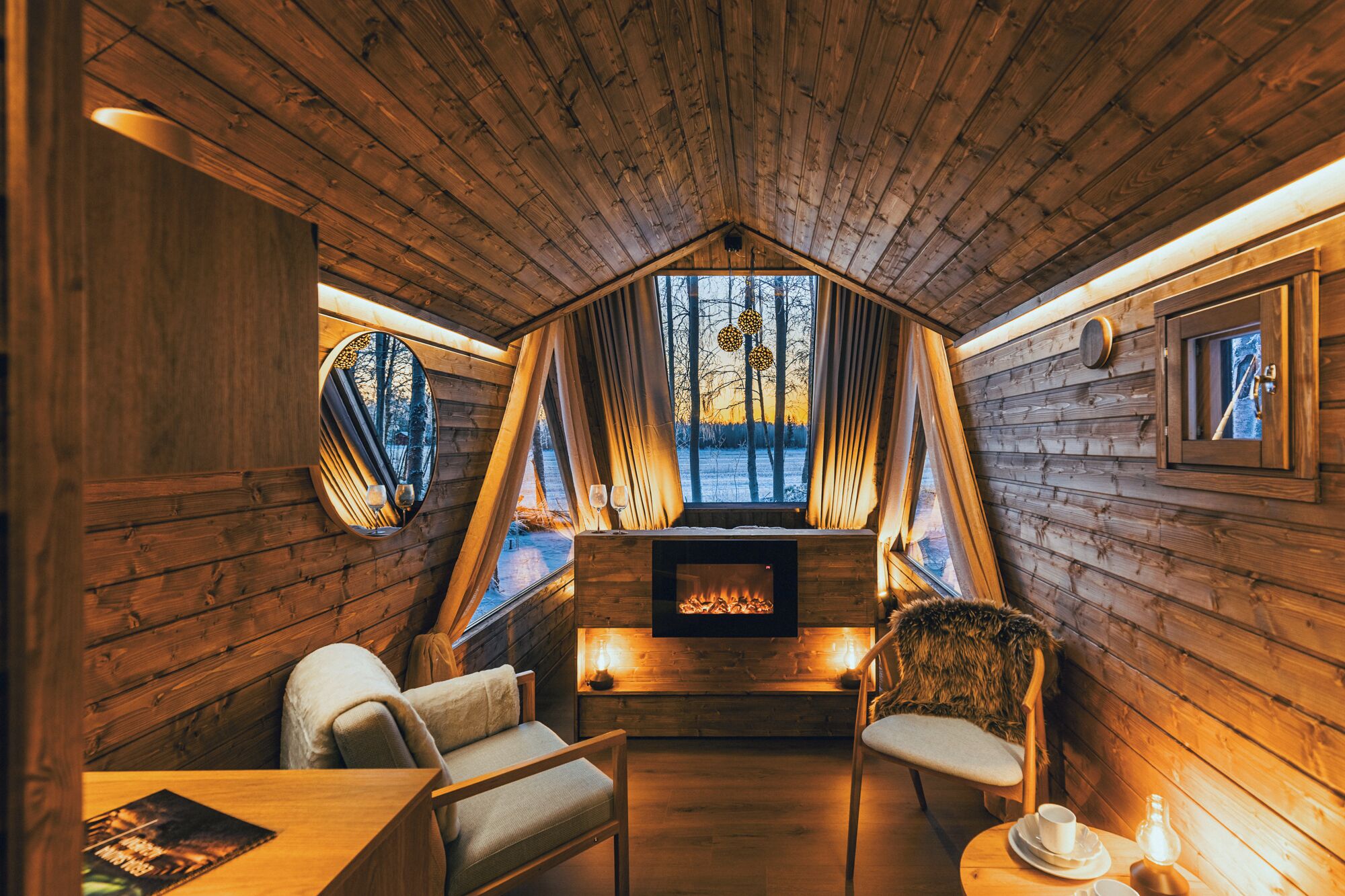 Ein gemütliches Blockhaus-Interieur mit Kamin, Holzwänden und Blick auf Bäume durch die Fenster.