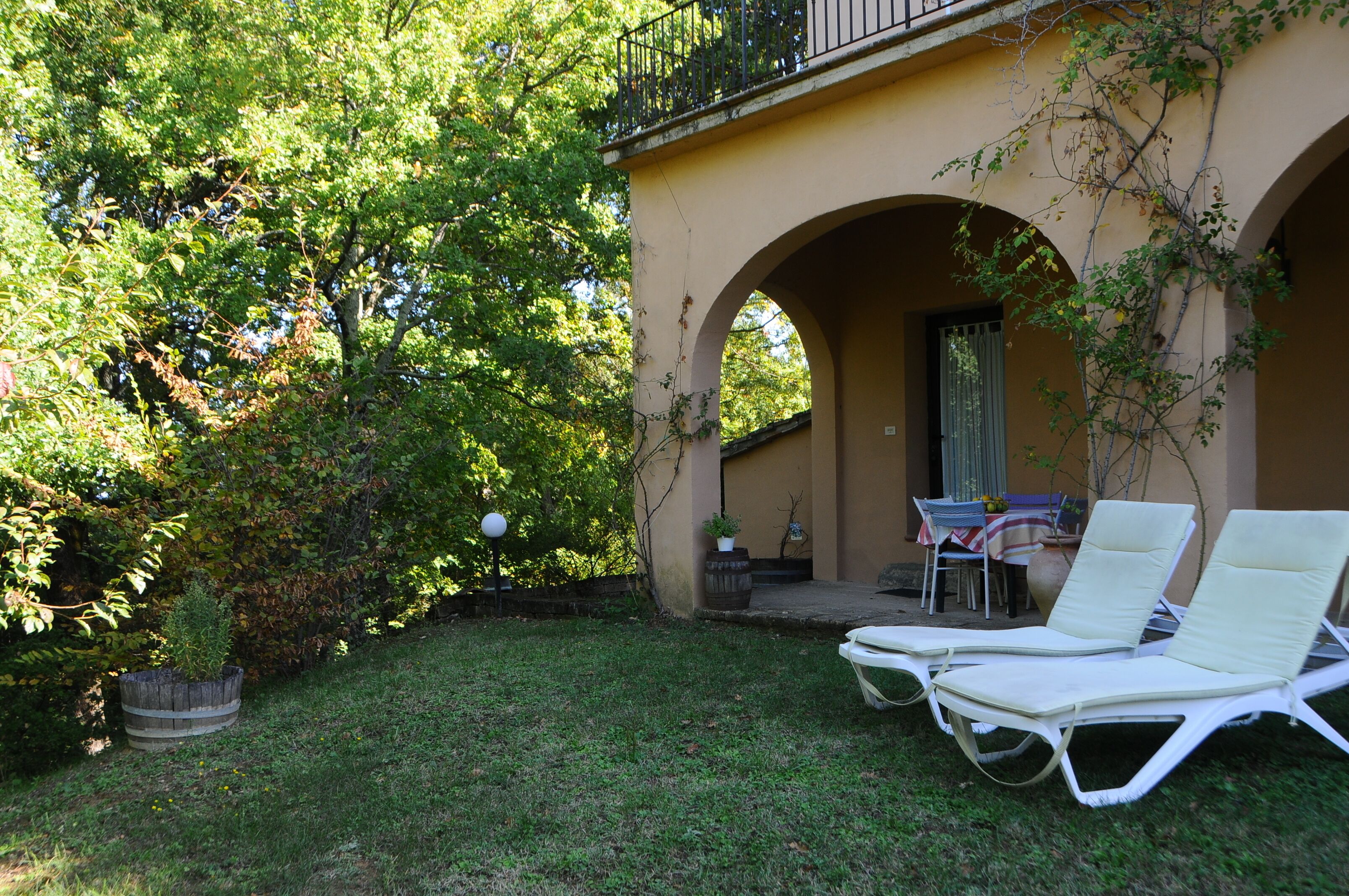A patio with two white lounge chairs, a table with chairs, and a small garden area with a tree and a planter.