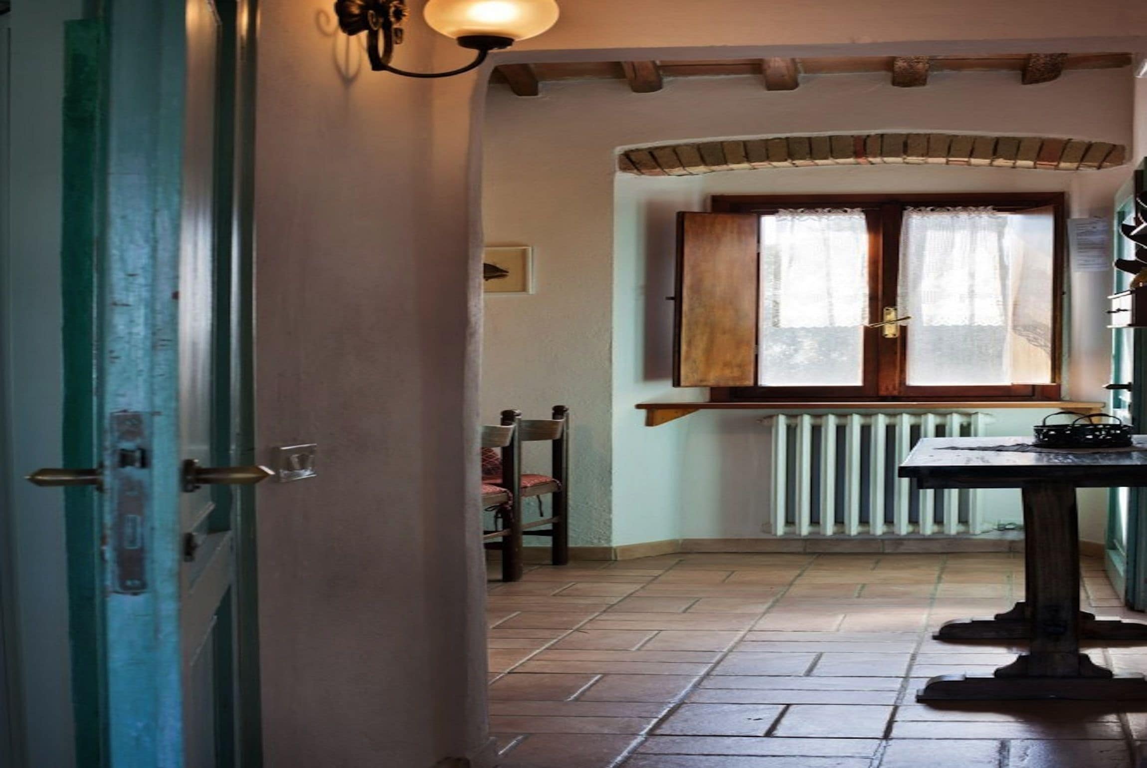A room with a wooden door, a radiator, a window with curtains, a table, and a chair.