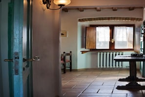 A room with a wooden door, a radiator, a window with curtains, a table, and a chair.