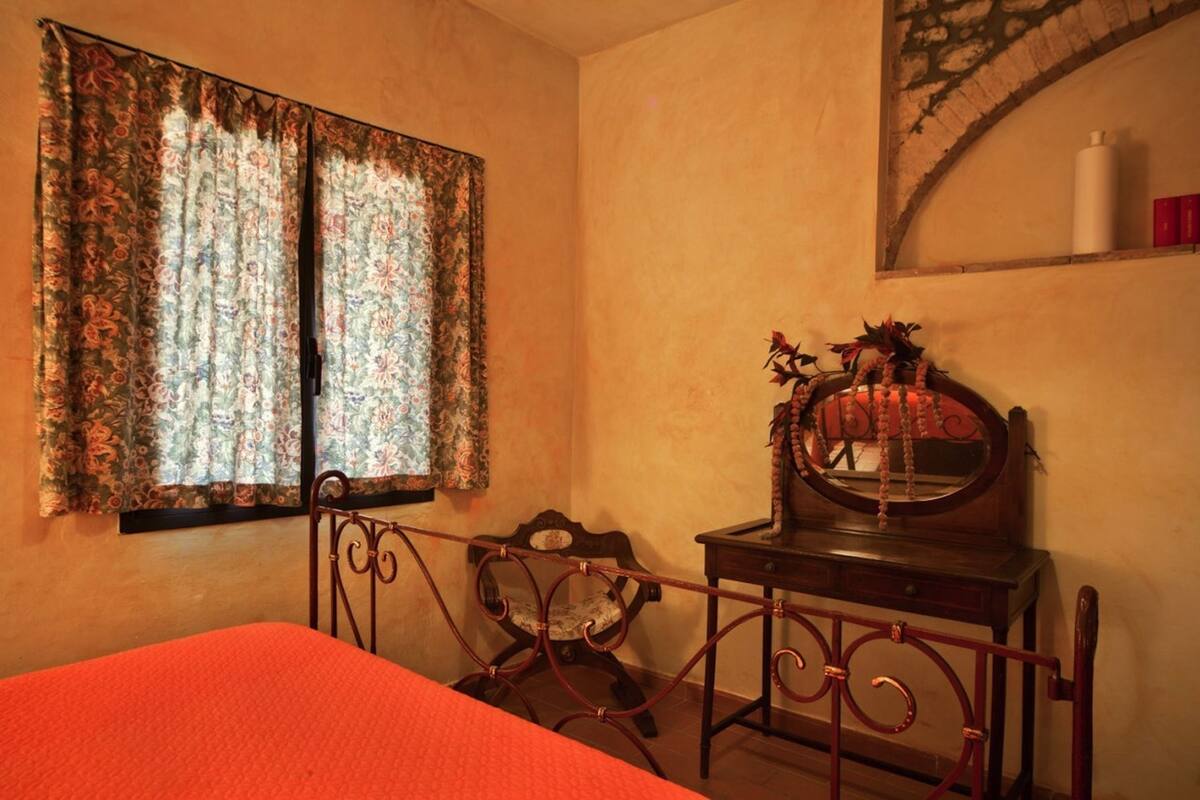 A bedroom with a bed, a chair, a dresser, a mirror, and a window with curtains.