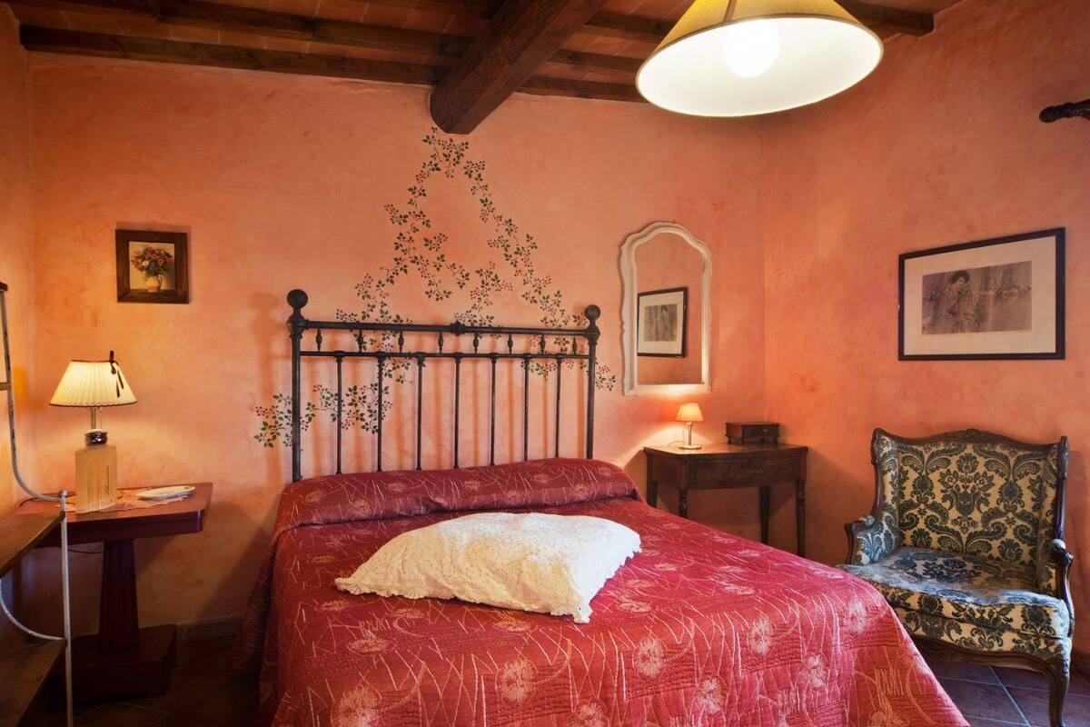A bedroom with a bed, a chair, a lamp, and a wall with a floral pattern.