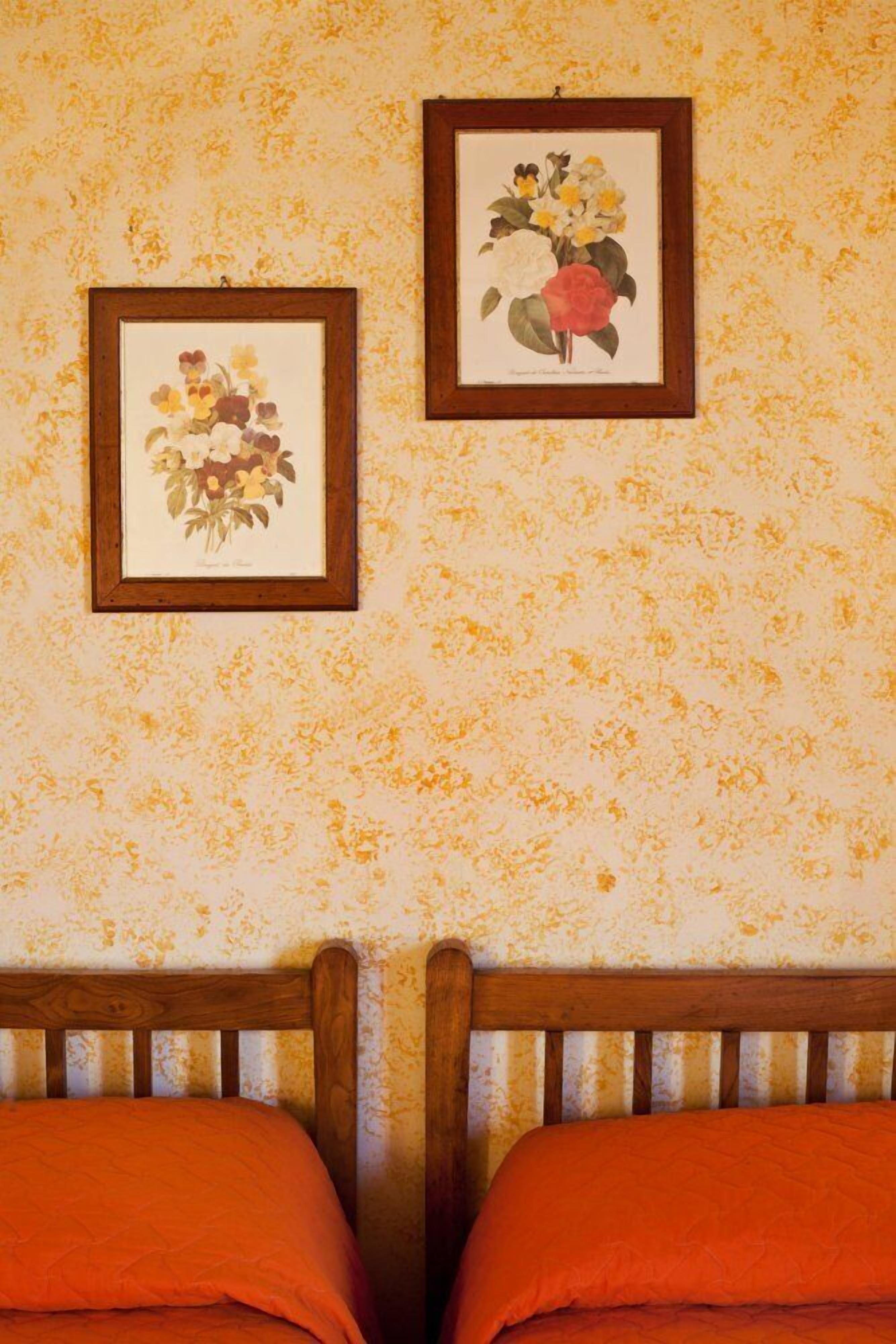 Une chambre avec deux lits, un papier peint à motifs floraux et deux reproductions botaniques encadrées accrochées au mur.