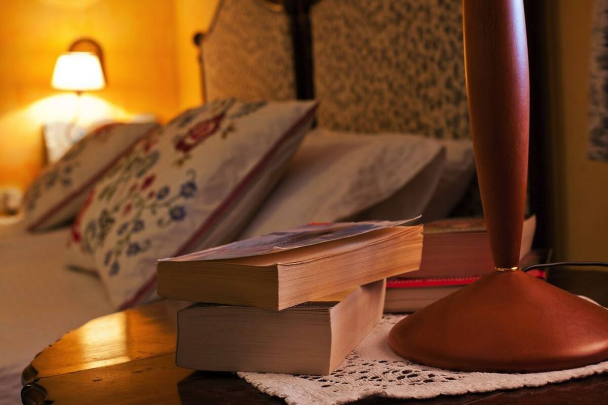 A bedside table with books, a lamp, and a patterned pillow.