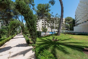 Un vialetto conduce a un edificio con area piscina, immerso nel verde e alberi.