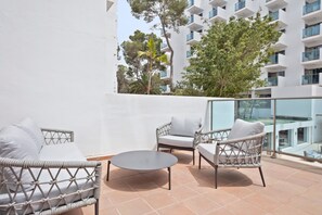 A balcony with wicker furniture, a round table, and a view of a modern building with balconies. - Hotel Best Delta (Llucmajor)