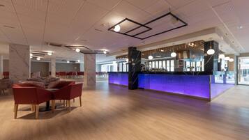 En modern hotellobby med en bardel, sittplatser och ett högt tak med belysningsarmaturer.