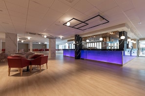 A modern hotel lobby with a bar area, seating, and a high ceiling with lighting fixtures. - Hotel Best Delta (Llucmajor)
