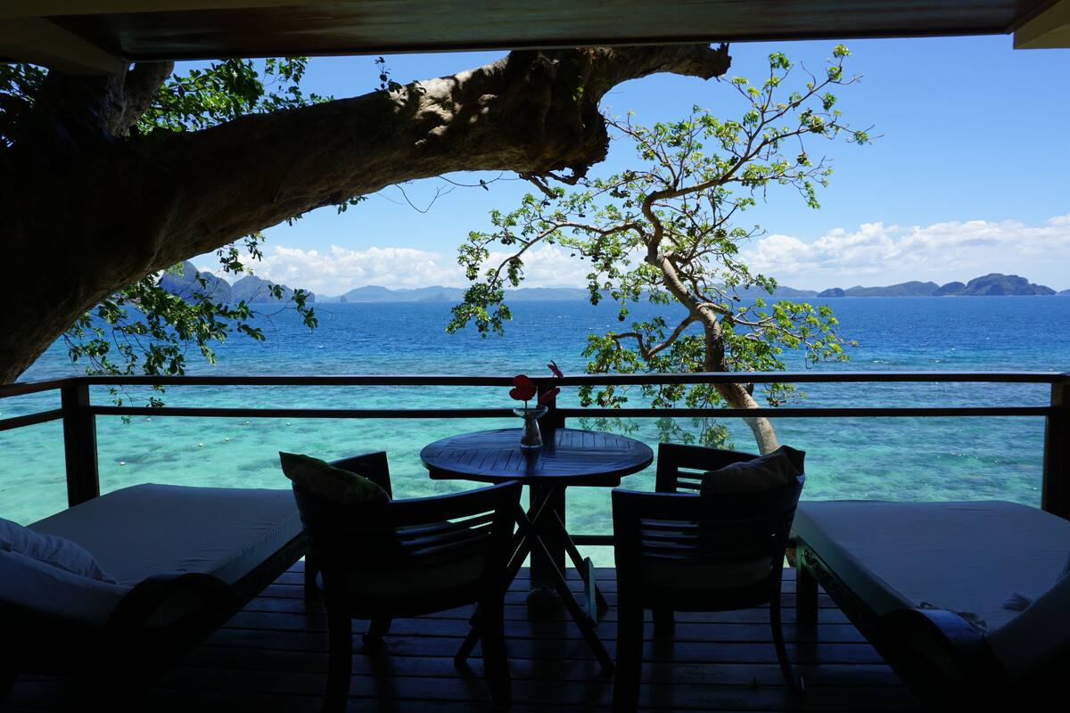 A deck with a table and chairs overlooking a body of water with mountains in the distance.