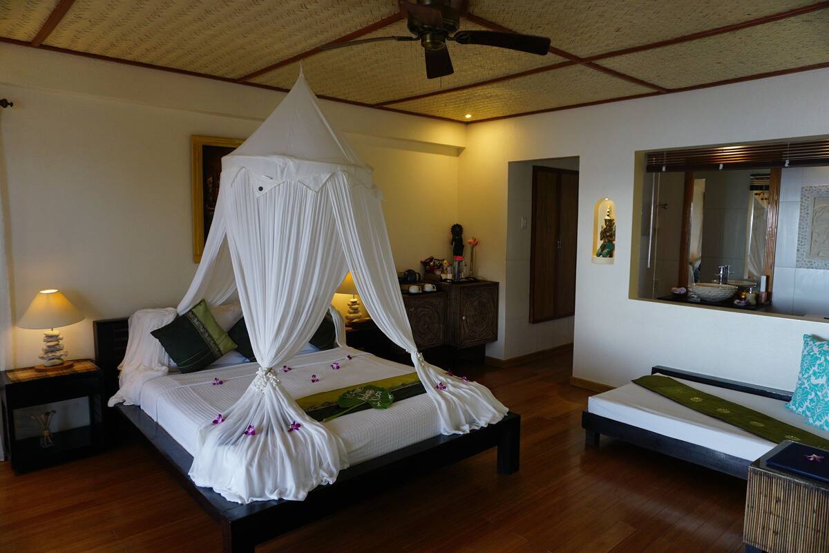 A bedroom with a four-poster bed, a bedside table with a lamp, a small cabinet, and a mirror on the wall.