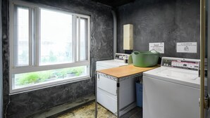 A laundry room with two washing machines, a drying rack, and a window with a view of greenery. - Work Inn TPE - Hostel (Taipei)