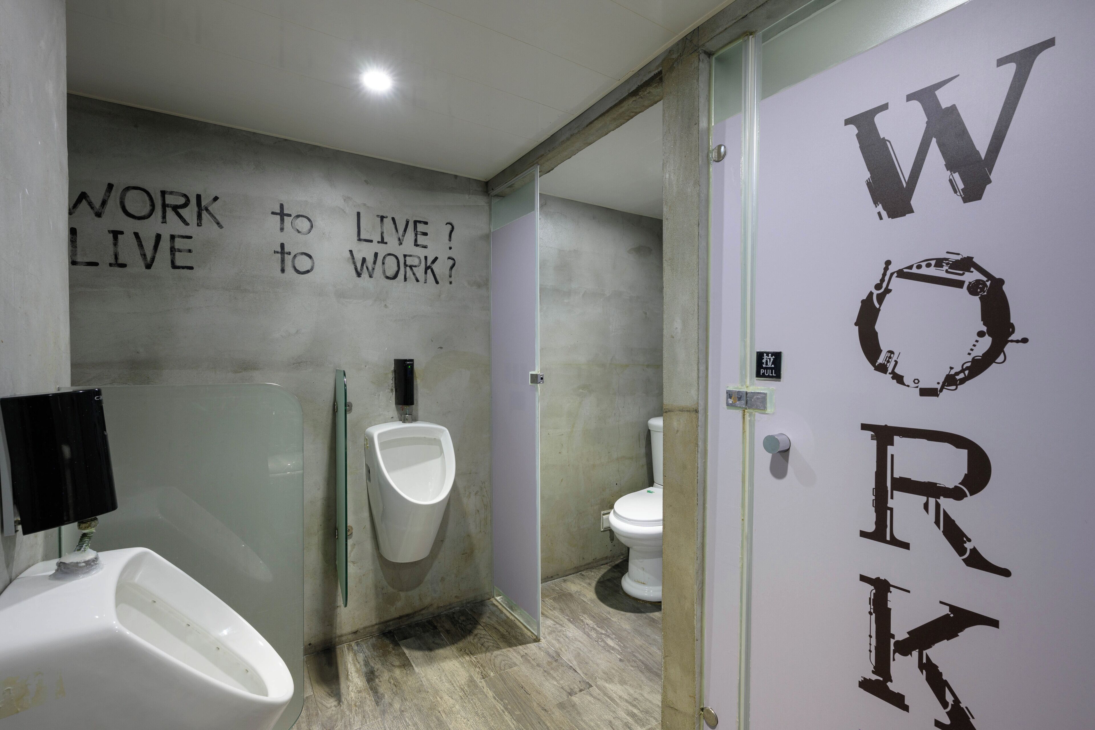 A modern bathroom with a urinal, toilet, and a wall with motivational text.