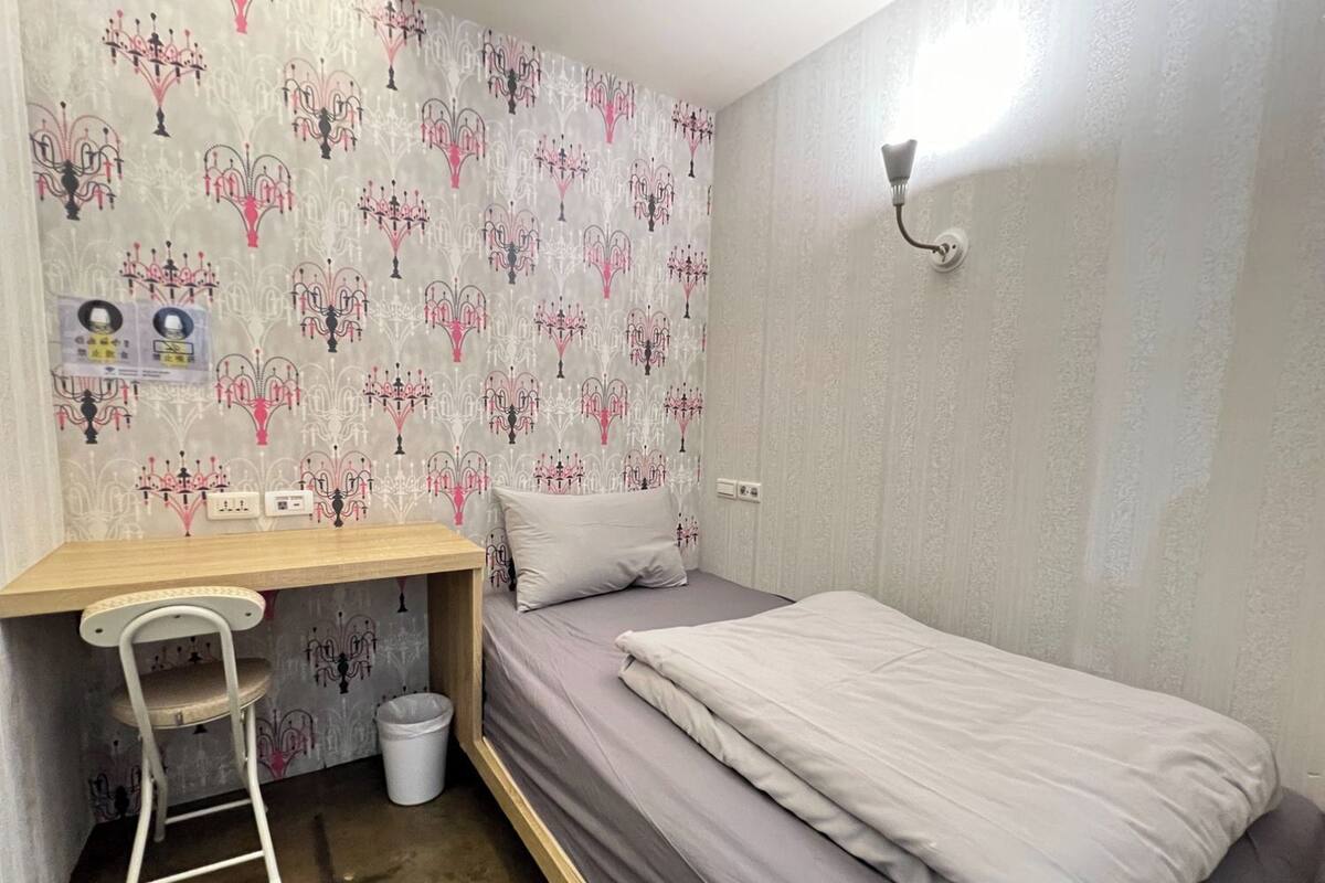 A small, tidy room with a single bed, a desk, and a chair.