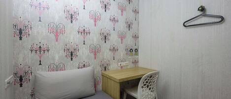 A small room with a bed, a desk, and a chair. There is a hanger on the wall.