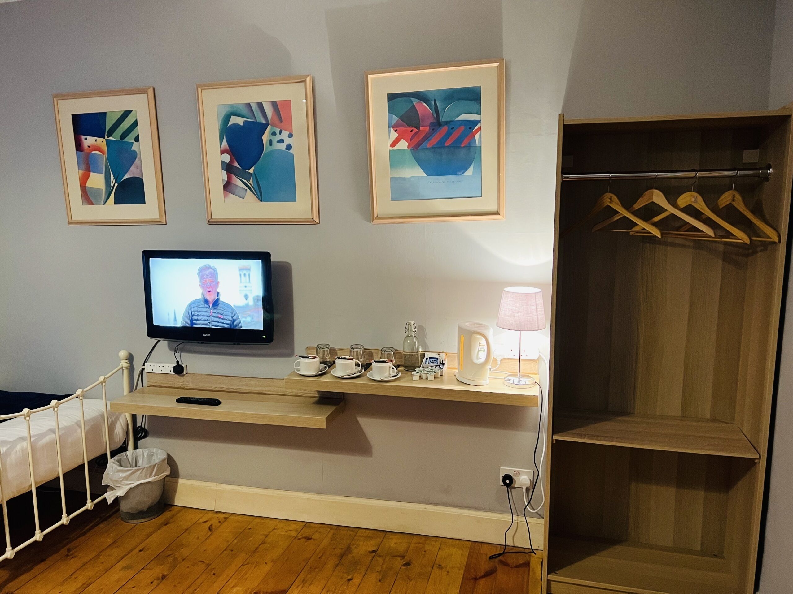 Ein Hotelzimmer mit Bett, Fernseher, Ablage mit Tassen und Wasserkocher sowie abstrakter Kunst an der Wand.