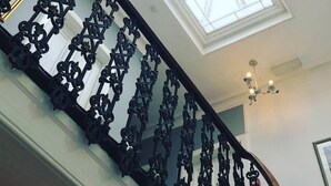 Una escalera con barandales negros ornamentados y un tragaluz arriba.