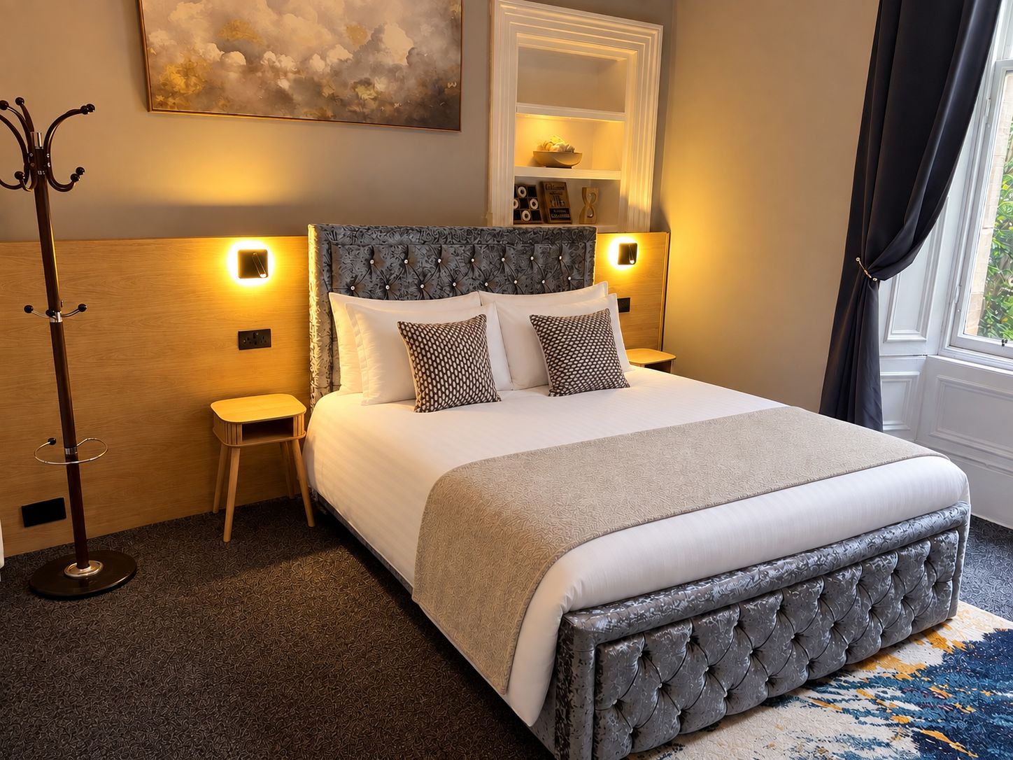 Habitación de hotel ordenada con una cama grande, mesitas de noche, perchero y un cuadro en la pared.