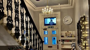 Una gran escalera con barandillas negras ornamentales, un candelabro y un reloj en la pared.